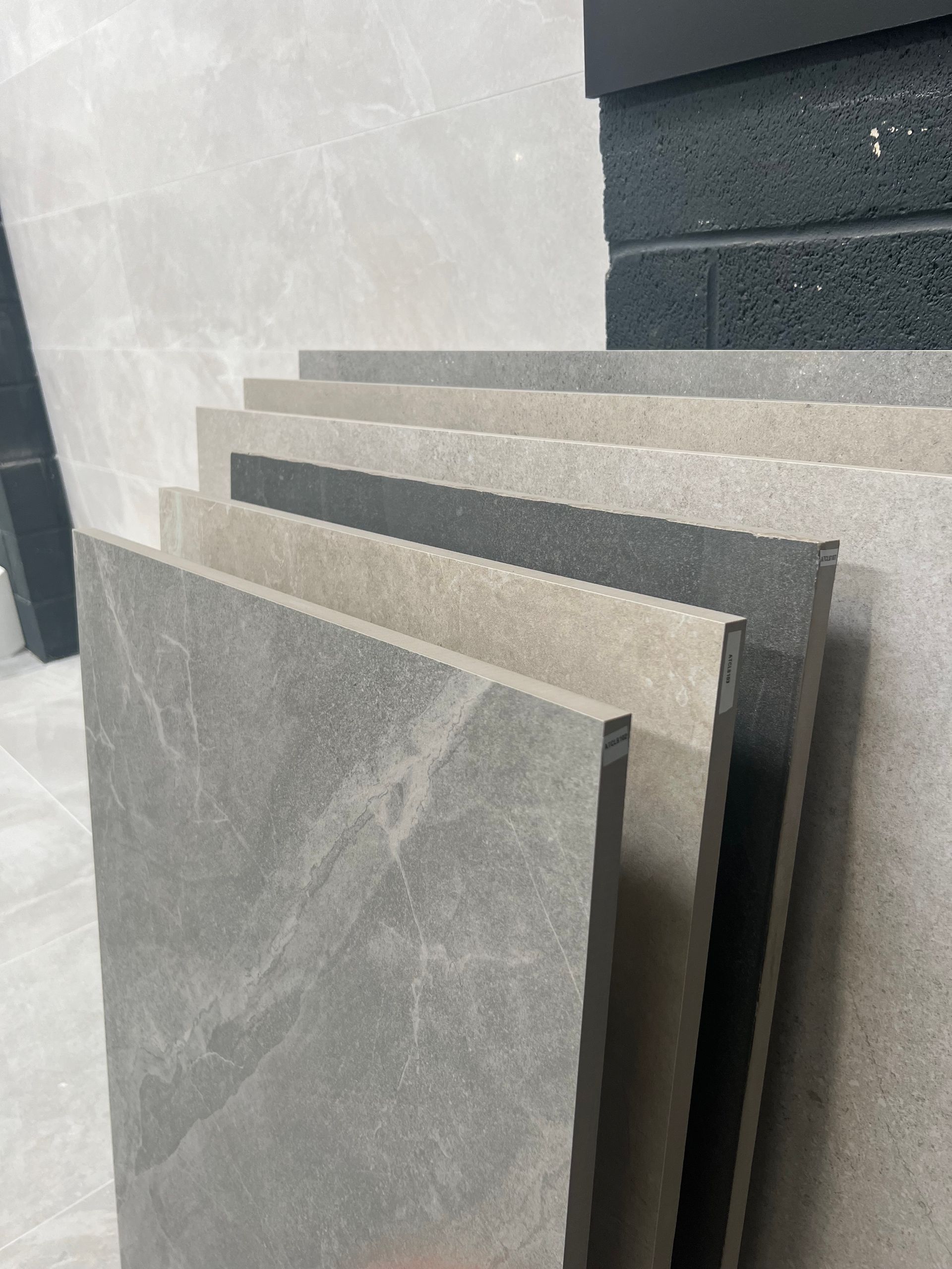 A selection of large format stone-effect porcelain tiles in various shades of grey and beige, displayed in a showroom.