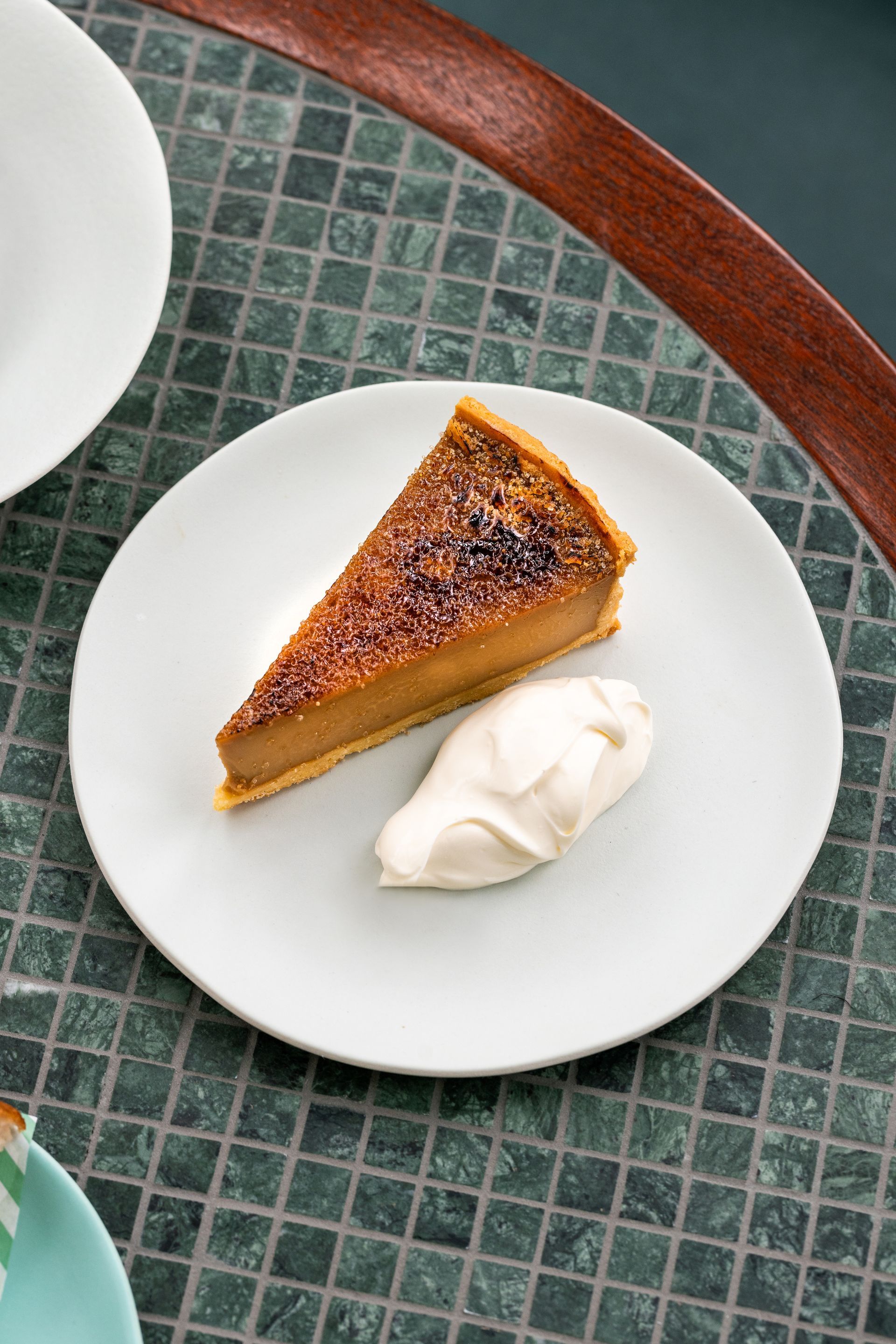 Pumpkin pie on a plate with cream under the plate you can see a custom made table with mosaic tiles grouted to make a table top