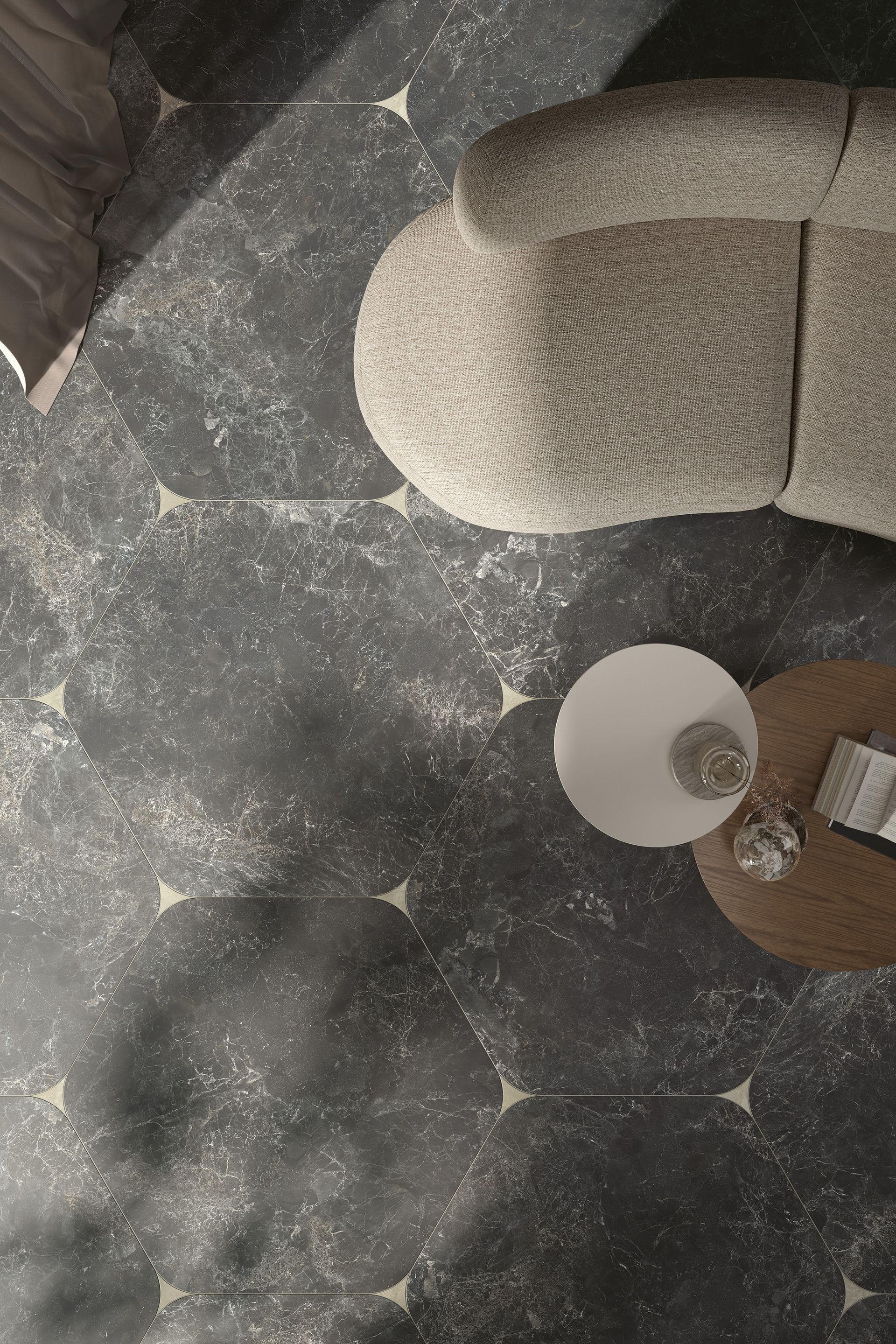 Overhead view of a stylish living room with dark hexagonal marble tiles featuring subtle veining. A beige, rounded armchair and a small round wooden side table with a glass vase and an open book are placed on the floor, creating a sophisticated and cozy atmosphere