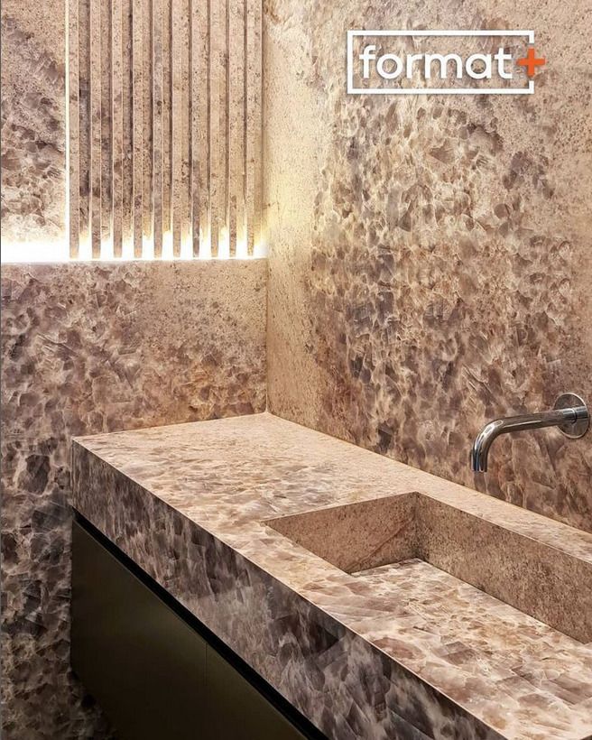 A close-up of a marble sink with subtle veining, set against a dark wall with a minimalistic design. The faucet is built into the wall for a seamless look.
