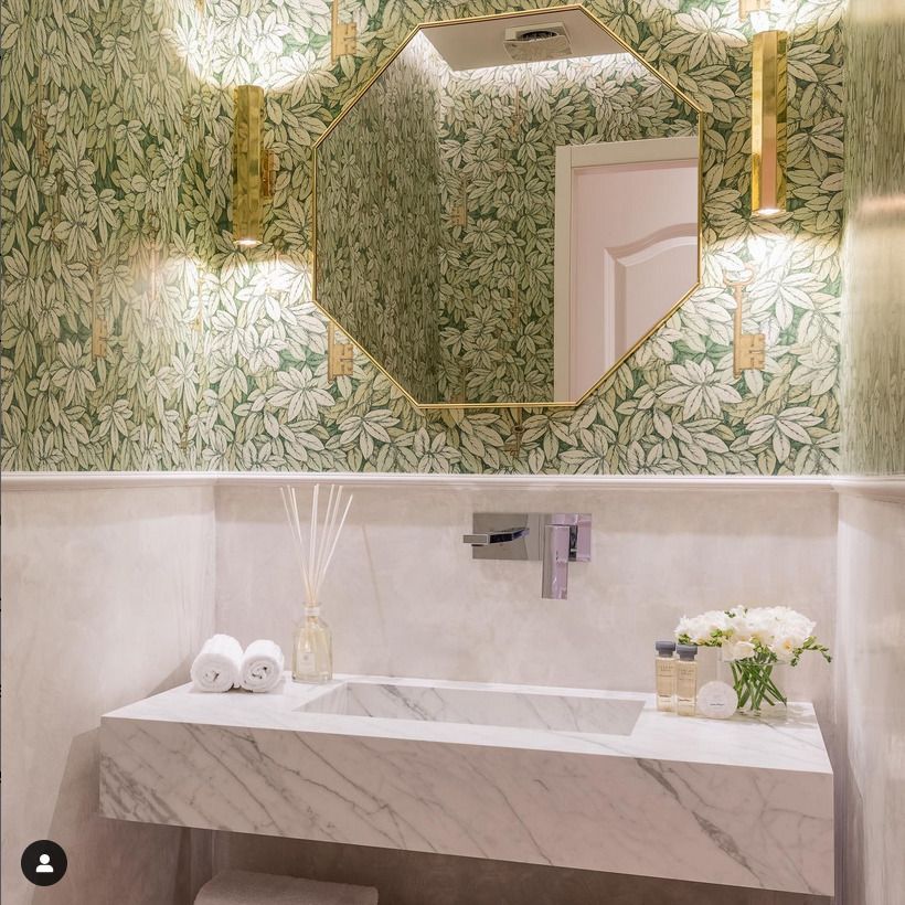 A detailed view of a bathroom featuring polished green marble walls and a countertop. The vibrant green tones are complemented by brass fixtures for a luxurious finish.