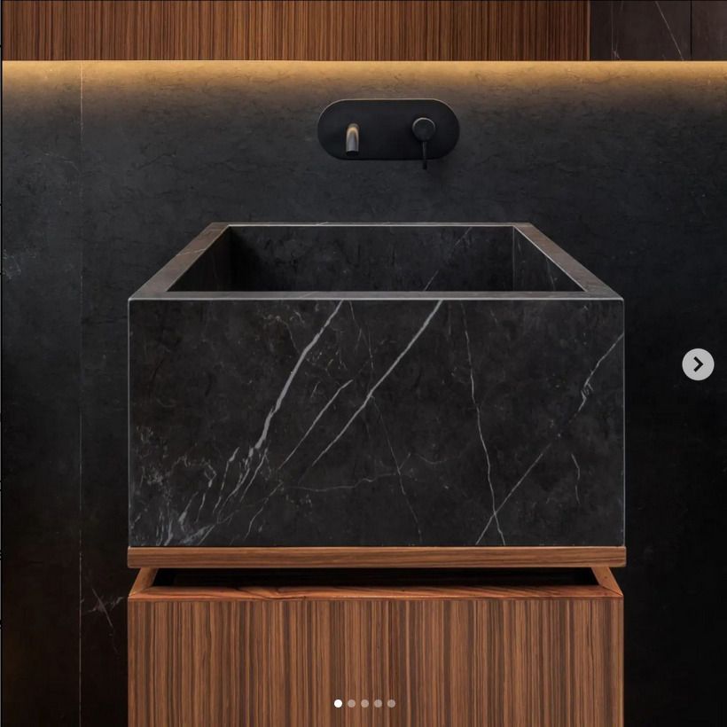 A close-up of a modern bathroom sink crafted from black marble with white veining, mounted on a wooden base. The sink features sleek, minimalist design with a black wall-mounted faucet.
