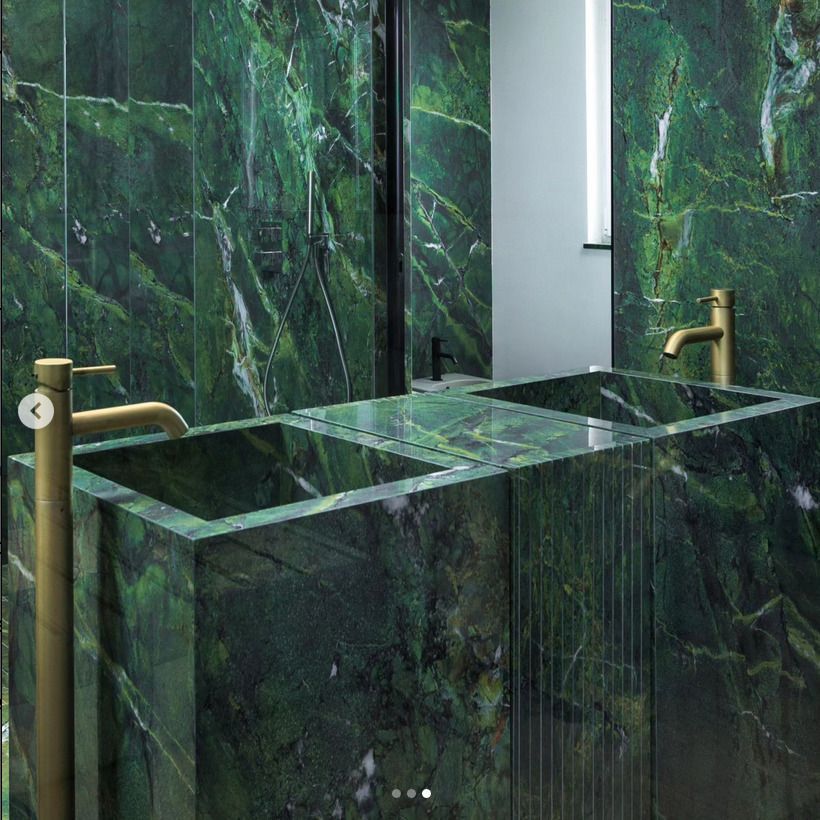 A luxurious bathroom featuring green marble walls and double sinks with matching green marble countertops. Gold faucets add a sophisticated contrast to the rich, green marble.