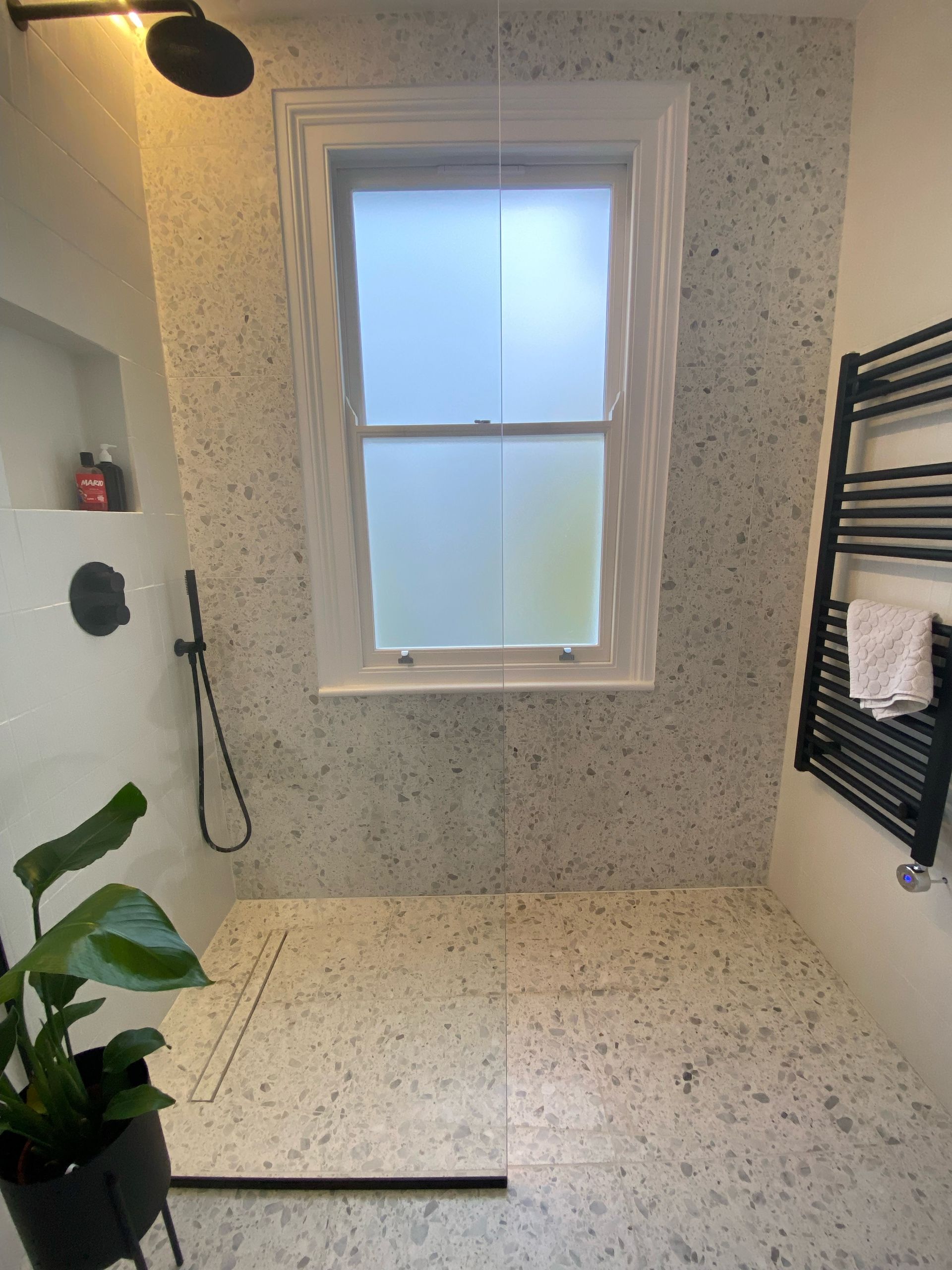 Real terrazzo in a shower with a black towel ral