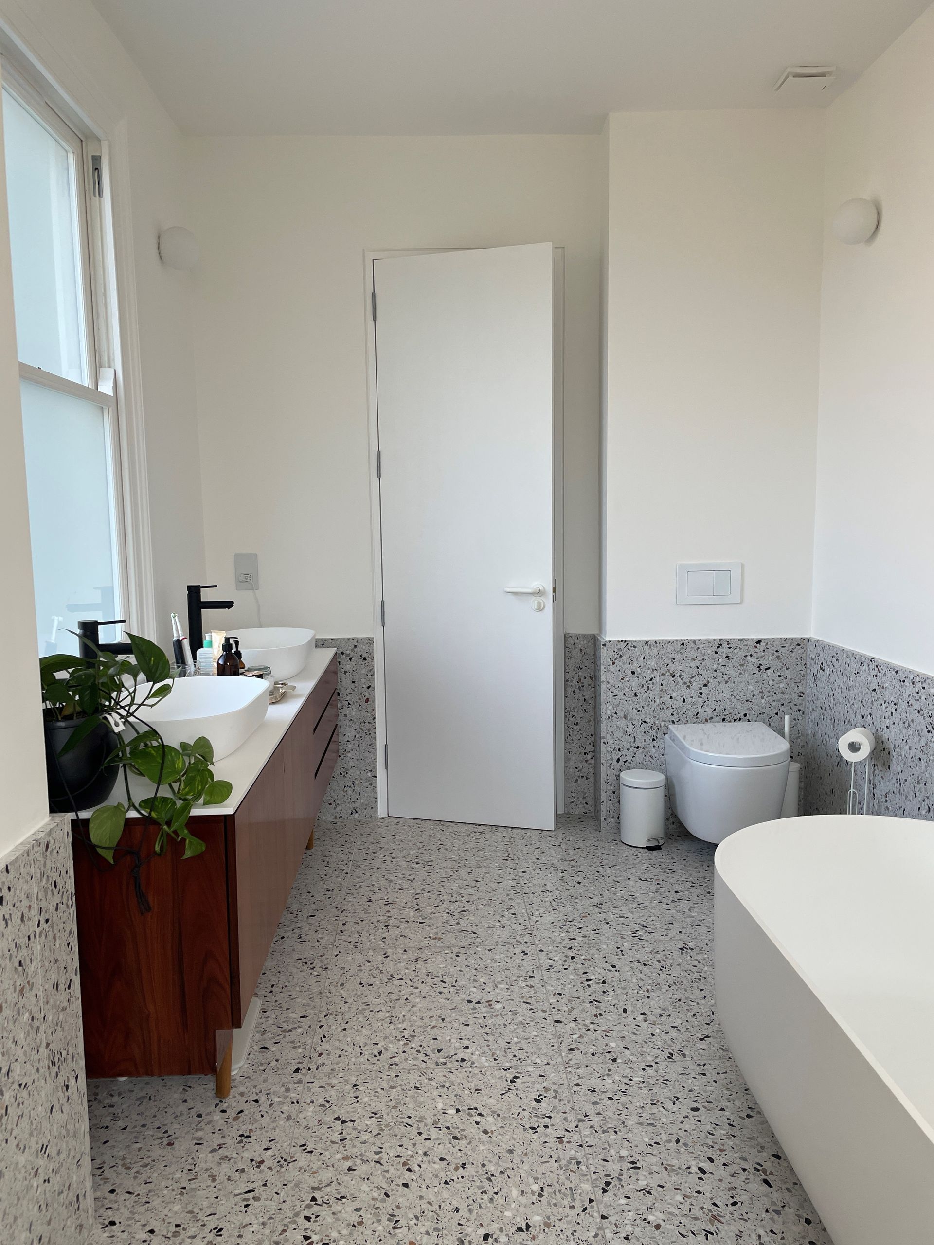 Terrazzo tiles on the floor and halfway up the wall with a wooden skink and white toilet