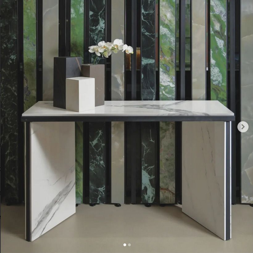 Marble console table with black accents, complemented by decor pieces and a backdrop of rich green marble tiles.