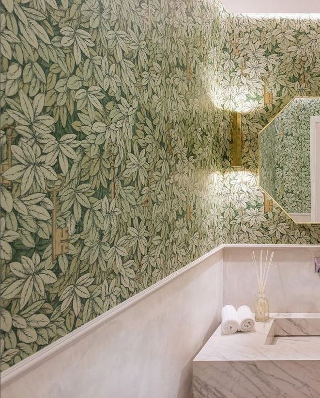 A bathroom vanity area featuring natural green foliage-patterned wallpaper with a marble sink and modern lighting, creating a tranquil ambiance.