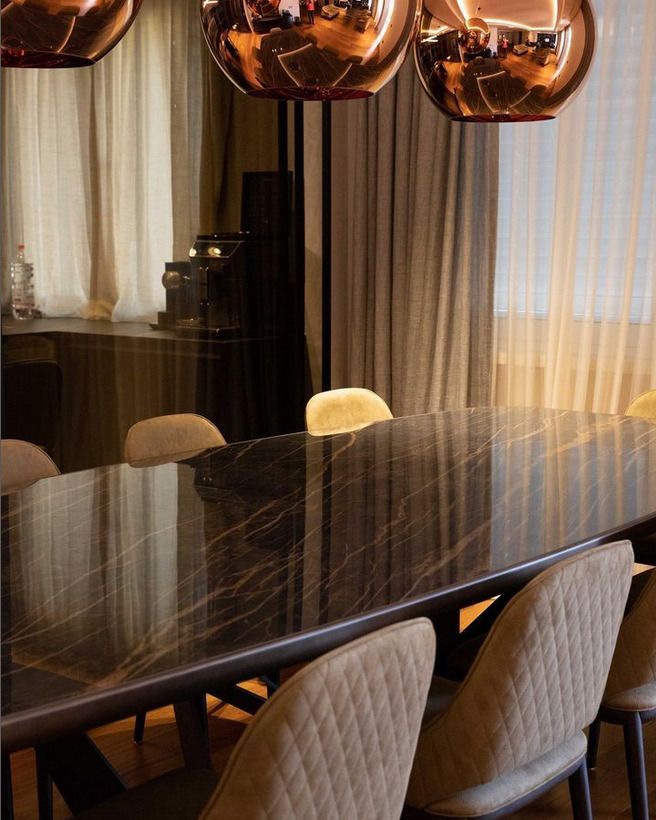 Dining room with a dark marble table and bronze pendant lighting, exuding modern luxury.