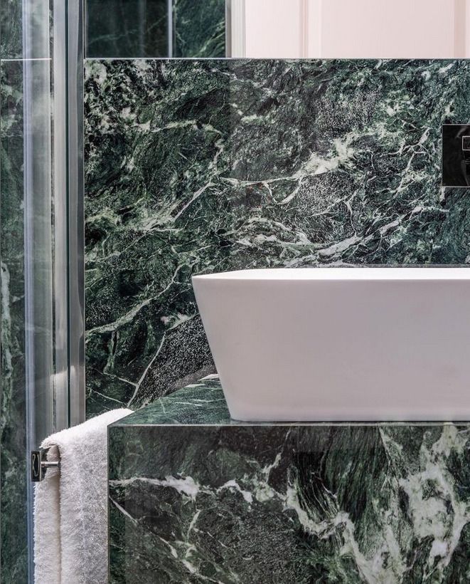 Shower area with rich green marble tiles surrounding a white bathtub, creating a luxurious feel.
