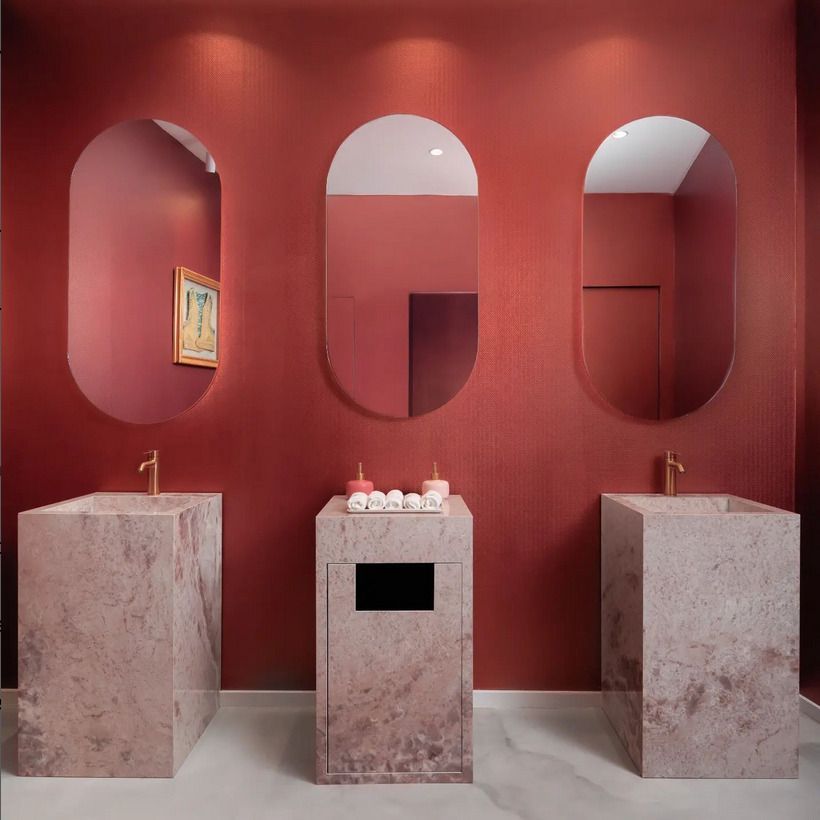 Modern bathroom with a bold red wall and matching stone vanities featuring arched mirrors.