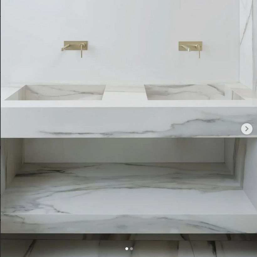 Minimalist white bathroom vanity with integrated sinks and gold fixtures, paired with a marble countertop.