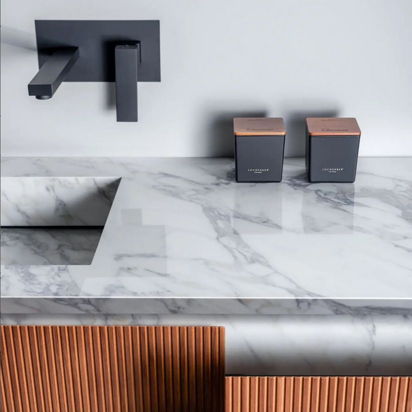 A luxurious marble countertop with a white and grey veined pattern, paired with black wall-mounted faucets, showcasing sleek bathroom design elements.