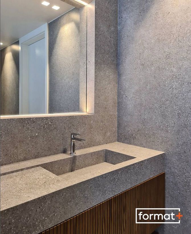 A contemporary bathroom vanity with a terrazzo-look countertop, featuring a minimalist faucet and warm lighting, with grey tiles in the background.