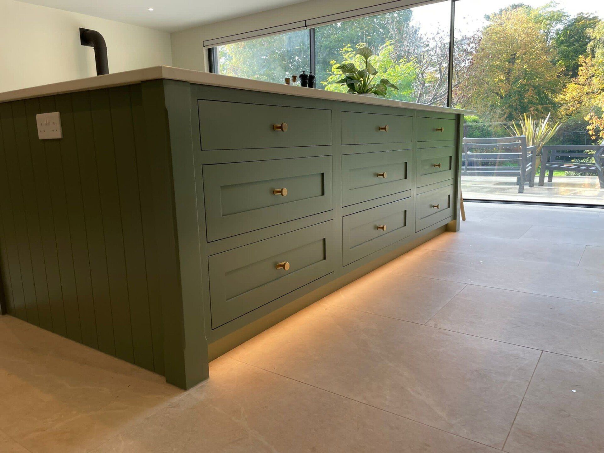 limestone effect tiles in a kitchen design with a green island and built in lights