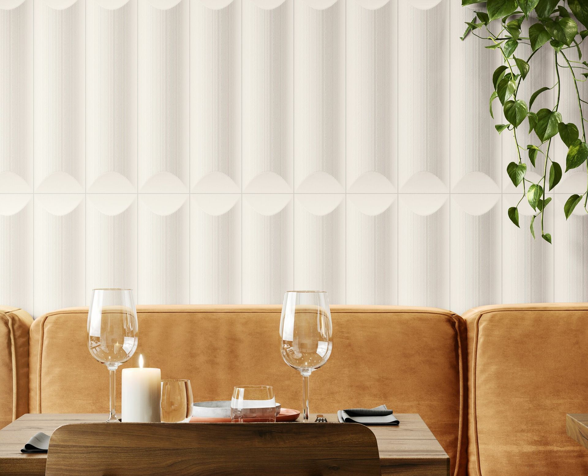 white feature wall tiles used in a restaurant with orangey yellow booth seats and high end wine glasses on the table with some fake plant ivy hanging down