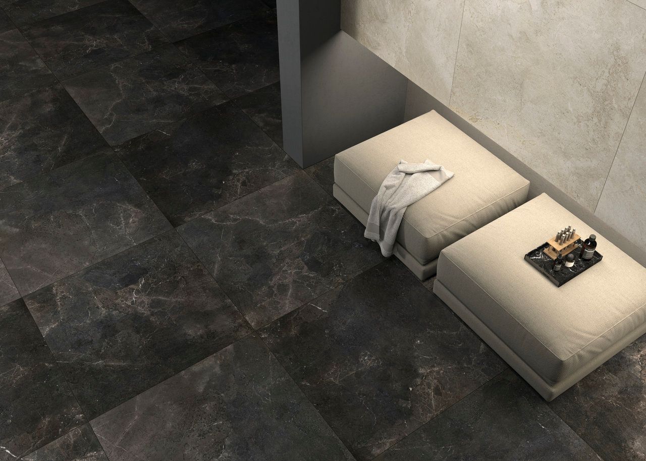 Lounge area with dark marble-look tiles and soft, beige ottomans. A folded throw and tray with small items on the ottoman add a touch of comfort to the luxurious, sleek space.