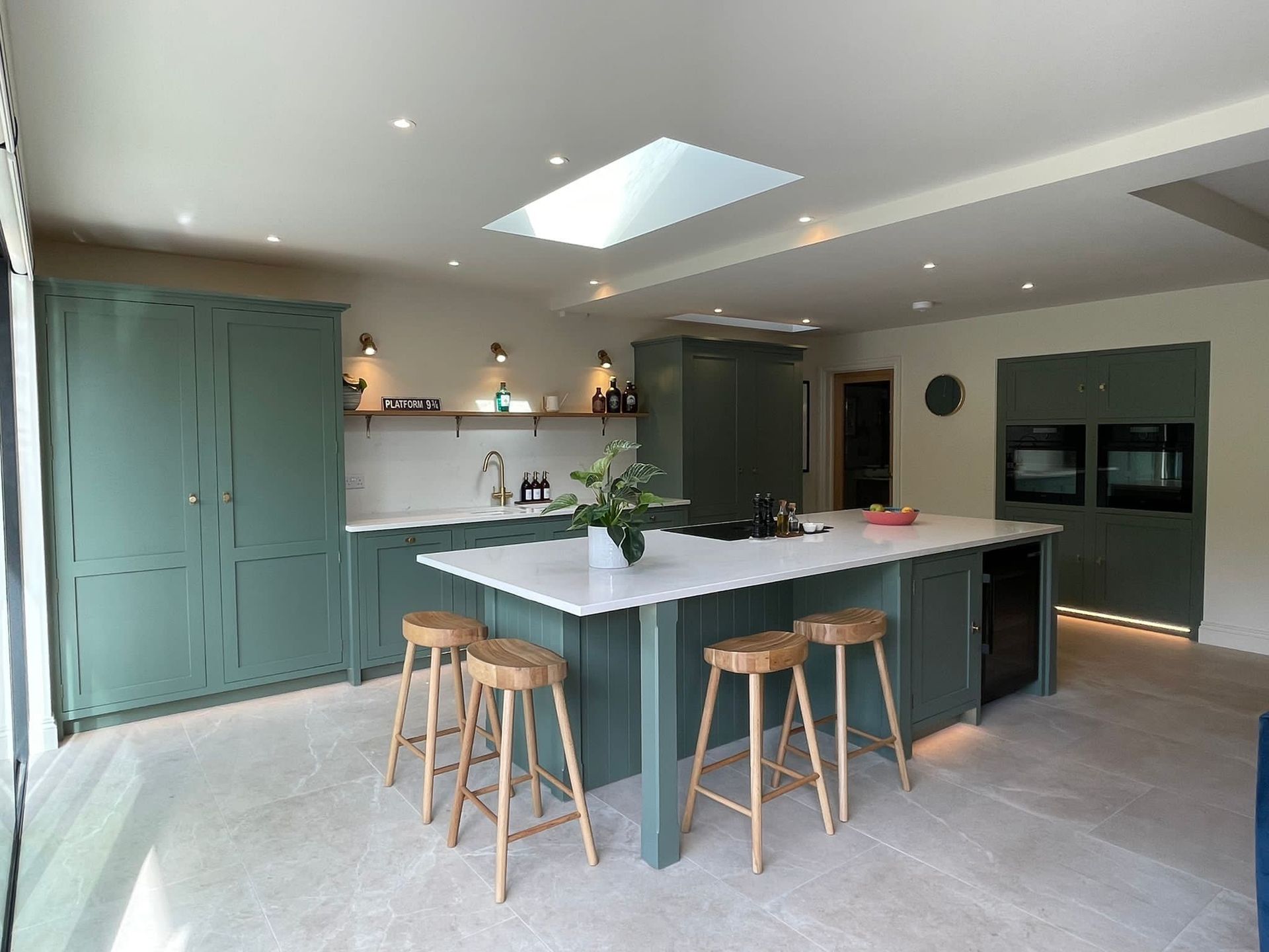 kitchen room shot with malvern tiles on the floor and green cupboards and a white marble island countertop