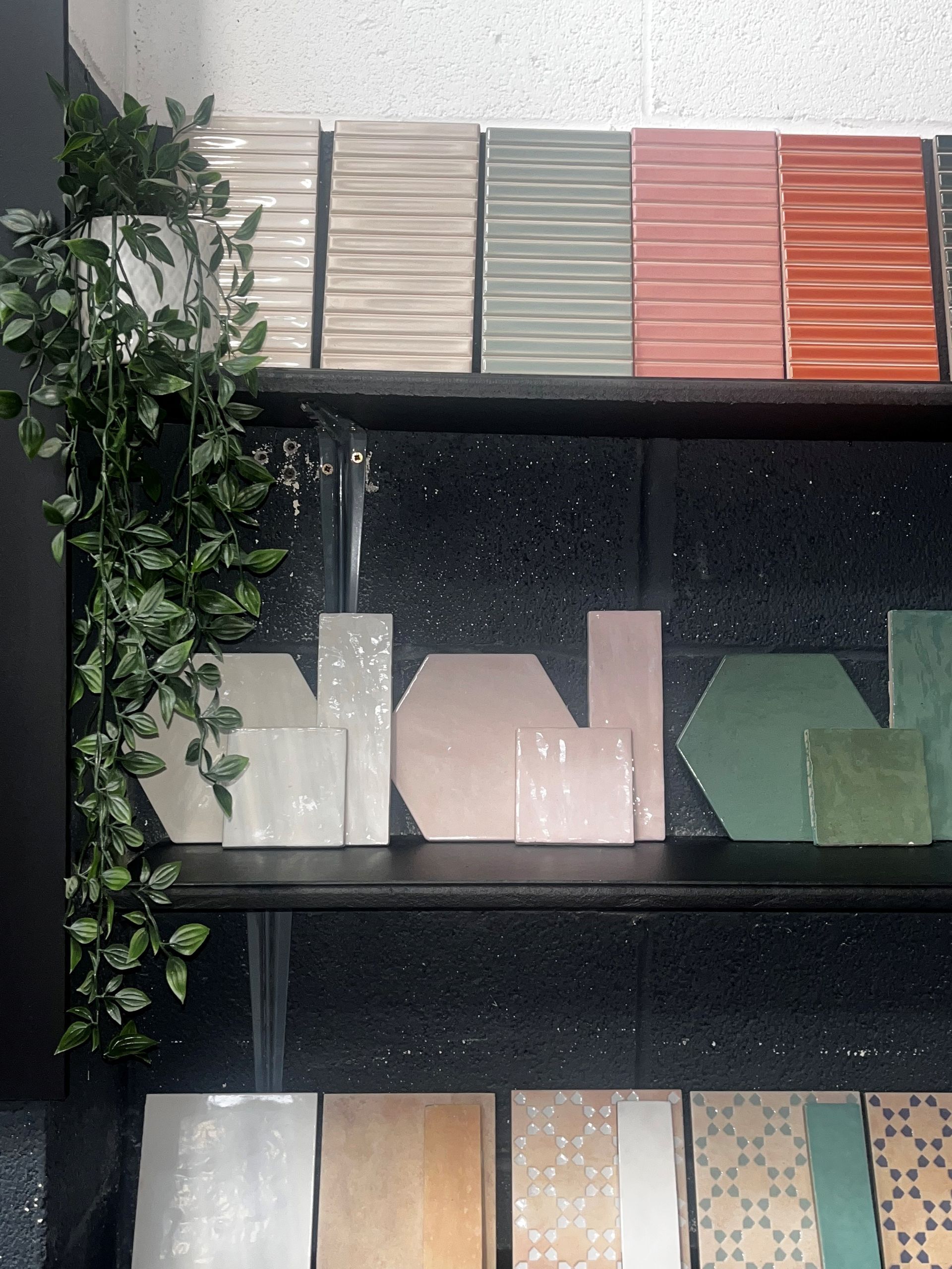 A display of various ceramic wall tiles in different pastel and neutral colors, including rectangular and hexagonal shapes, arranged on shelves.