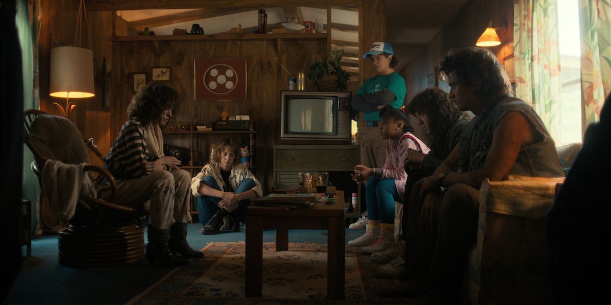from left to right, Nancy, Robin, Dustin, Erica, Eddie, Steve all sat around in living area in Eddie's uncles trailer.