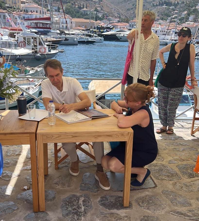 Jeff Koons illustrating and signing a copy of his artbook Apollo for Kelsey Edwards on Hydra Island