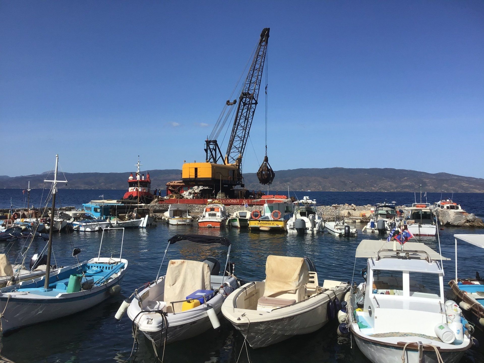 Sea crane-barge delivering stone to repair Kamini Harbour on Hydra Island Greece.