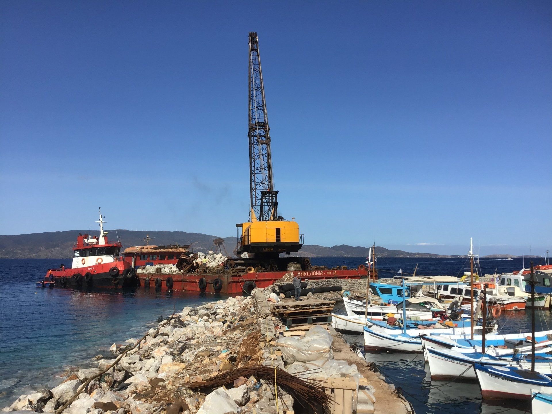 Sea crane-barge delivering stone to repair Kamini Harbour on Hydra Island Greece.