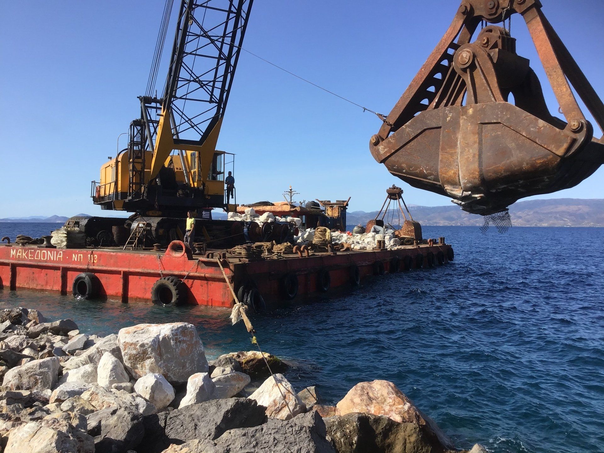 Sea crane-barge delivering stone to repair Kamini Harbour on Hydra Island Greece.