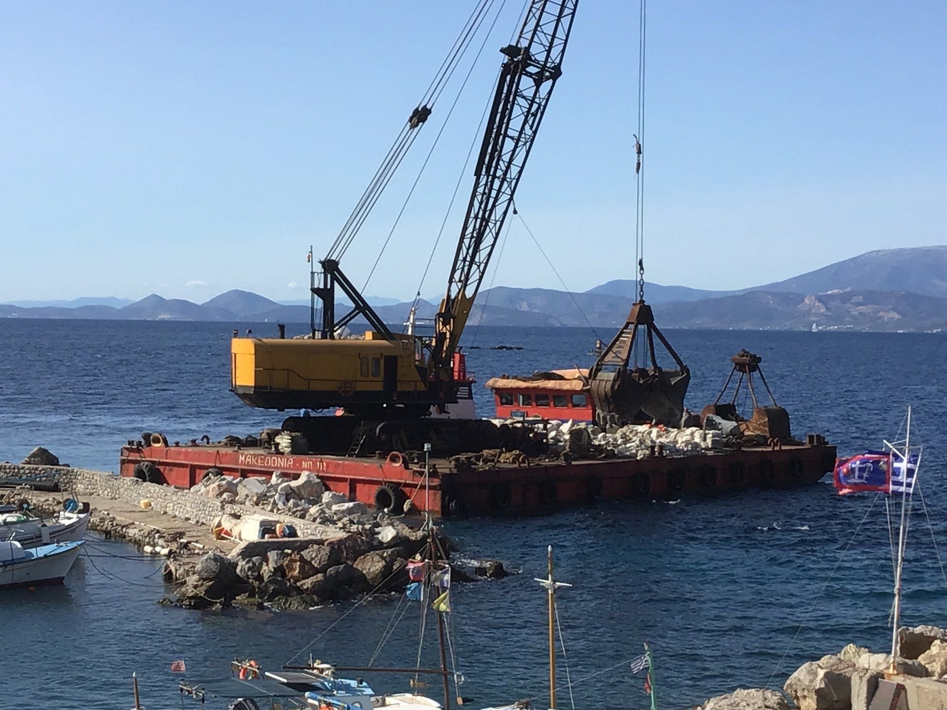 Sea crane-barge delivering stone to repair Kamini Harbour on Hydra Island Greece.