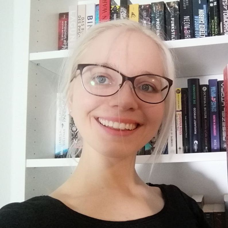 Swantje Niemann vor einem Bücherregal; sie hat hellblond gefärbte Haare und trägt eine dunkle Brille. Hinter ihr sind Science-Fiction-Romane zu sehen.