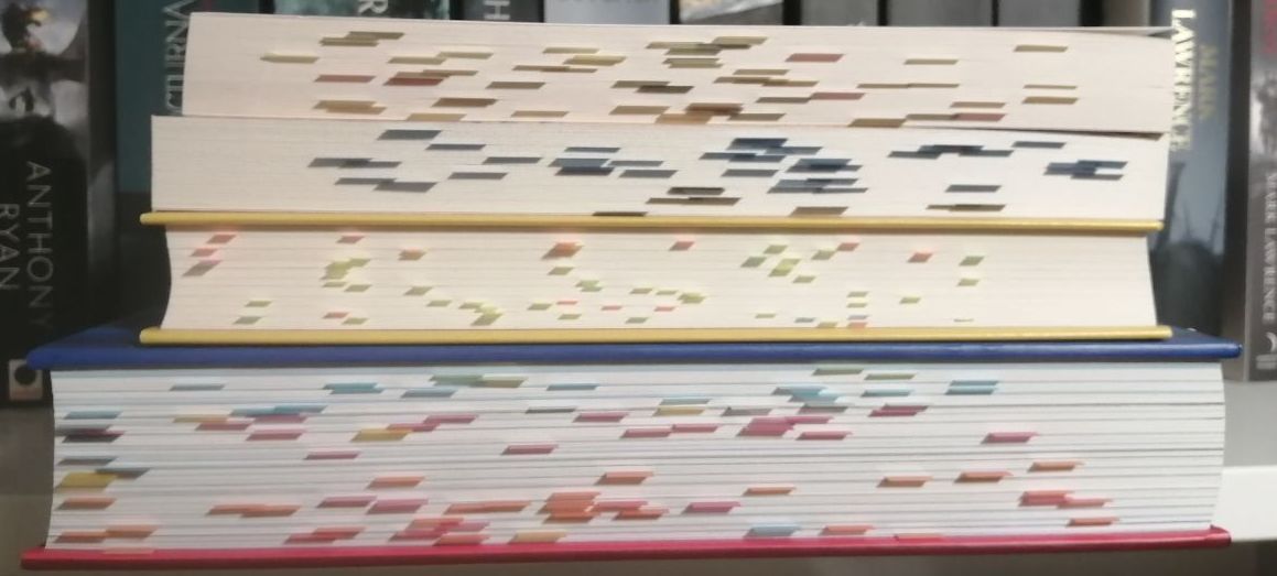 Stapel aus vier Büchern mit dem Schnitt nach vorne, zwischen den Seiten stecken zahlreiche Post-its.