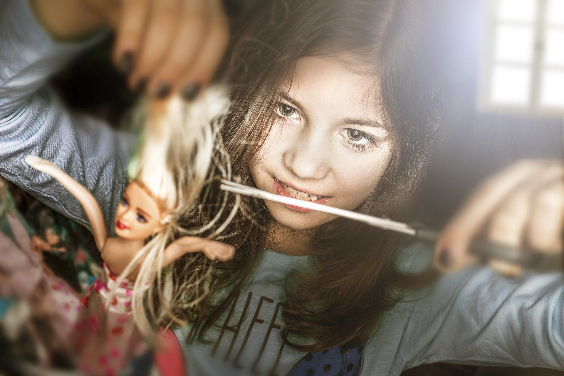 Kreatives Kinderportrait von einem Mädchen das einer Barbie die Haare abschneidet