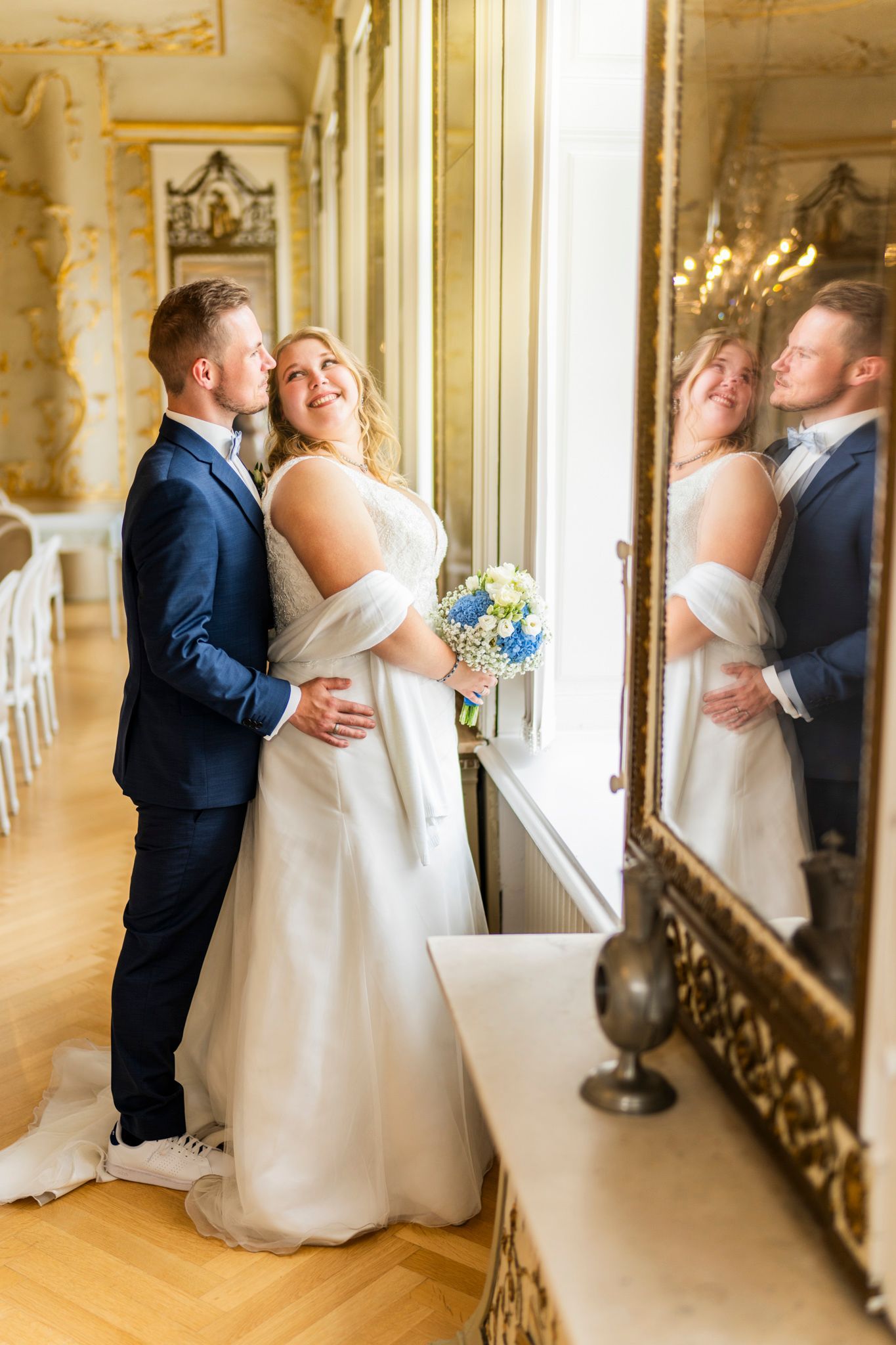 Brautpaar mit blauem Strauß am Fenster des Spiegelsaals in Wilster