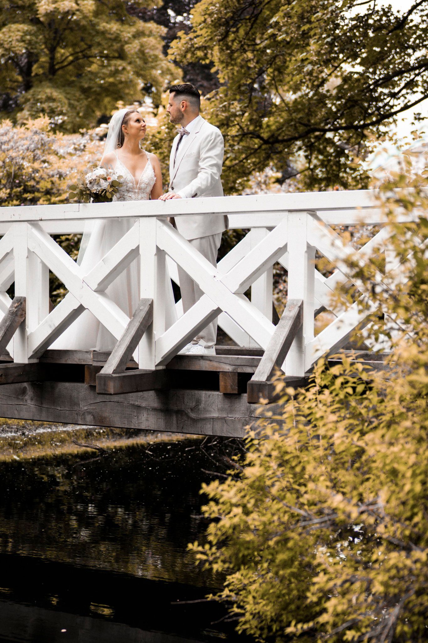 Brautpaar steht auf der weißen Holzbrücke zur Hochzeitsinsel in Uetersen