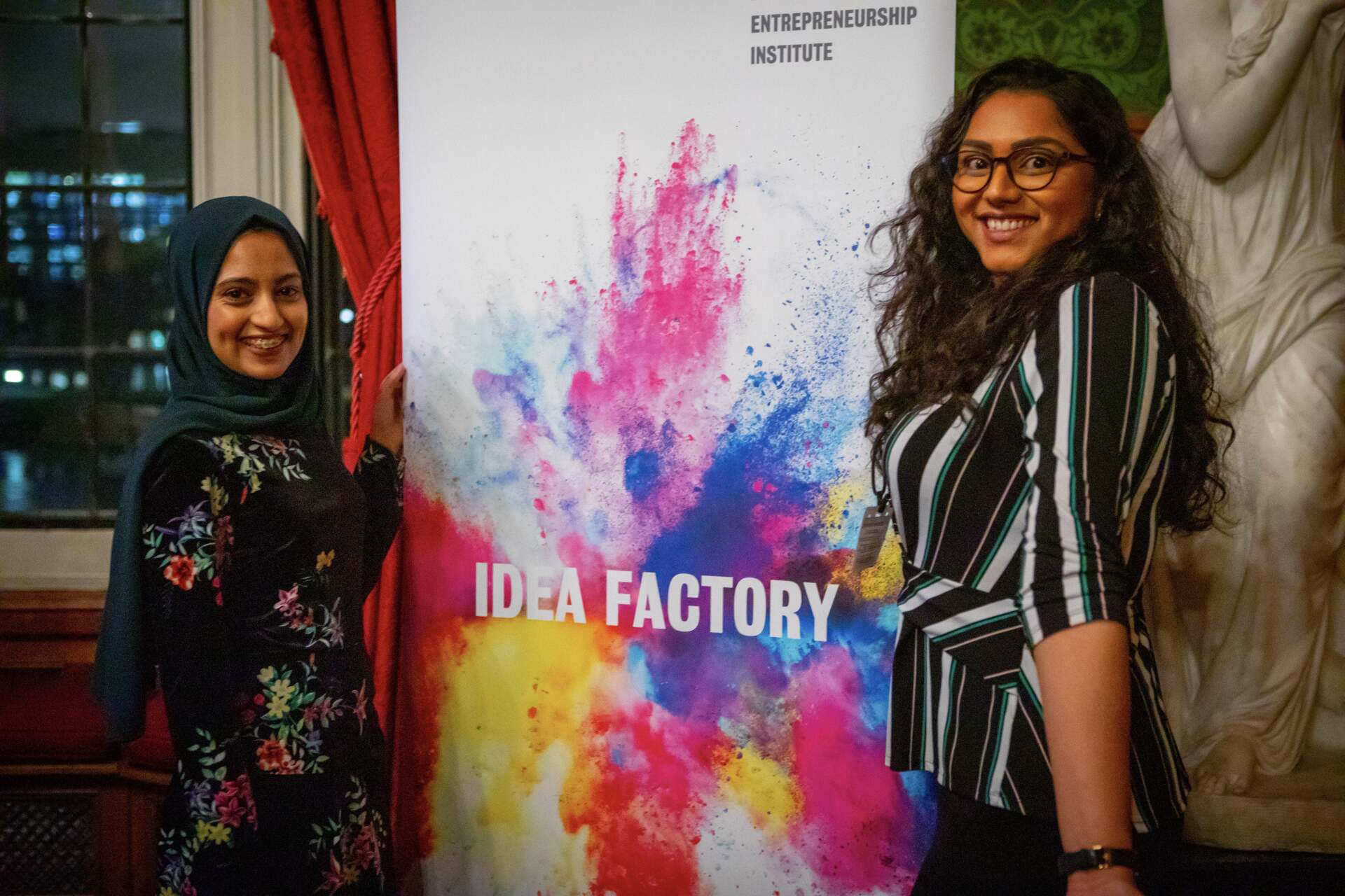 Aysha and King's Entrepreneurship Institute Leader posing in front of Ideas Factory Banner