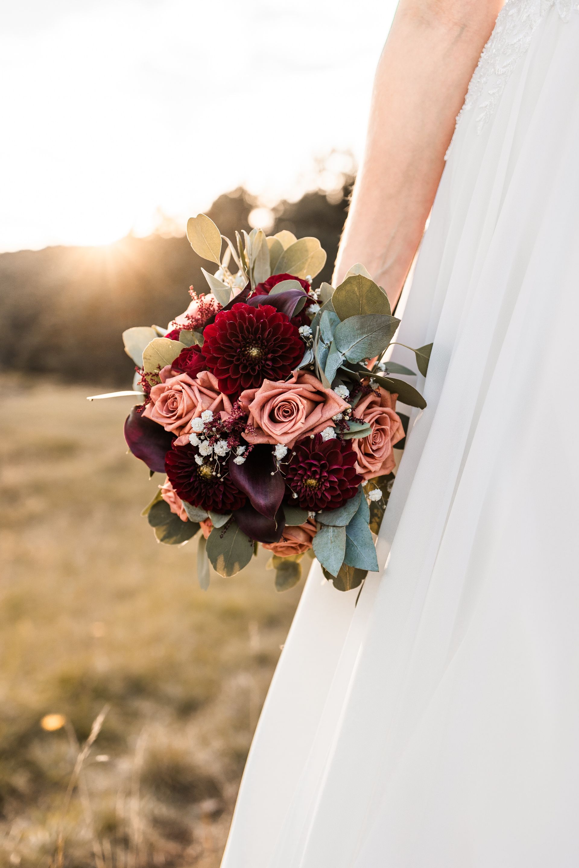 Auf diesem Foto sieht man einen roten Brautstrauß im Sonnenuntergang