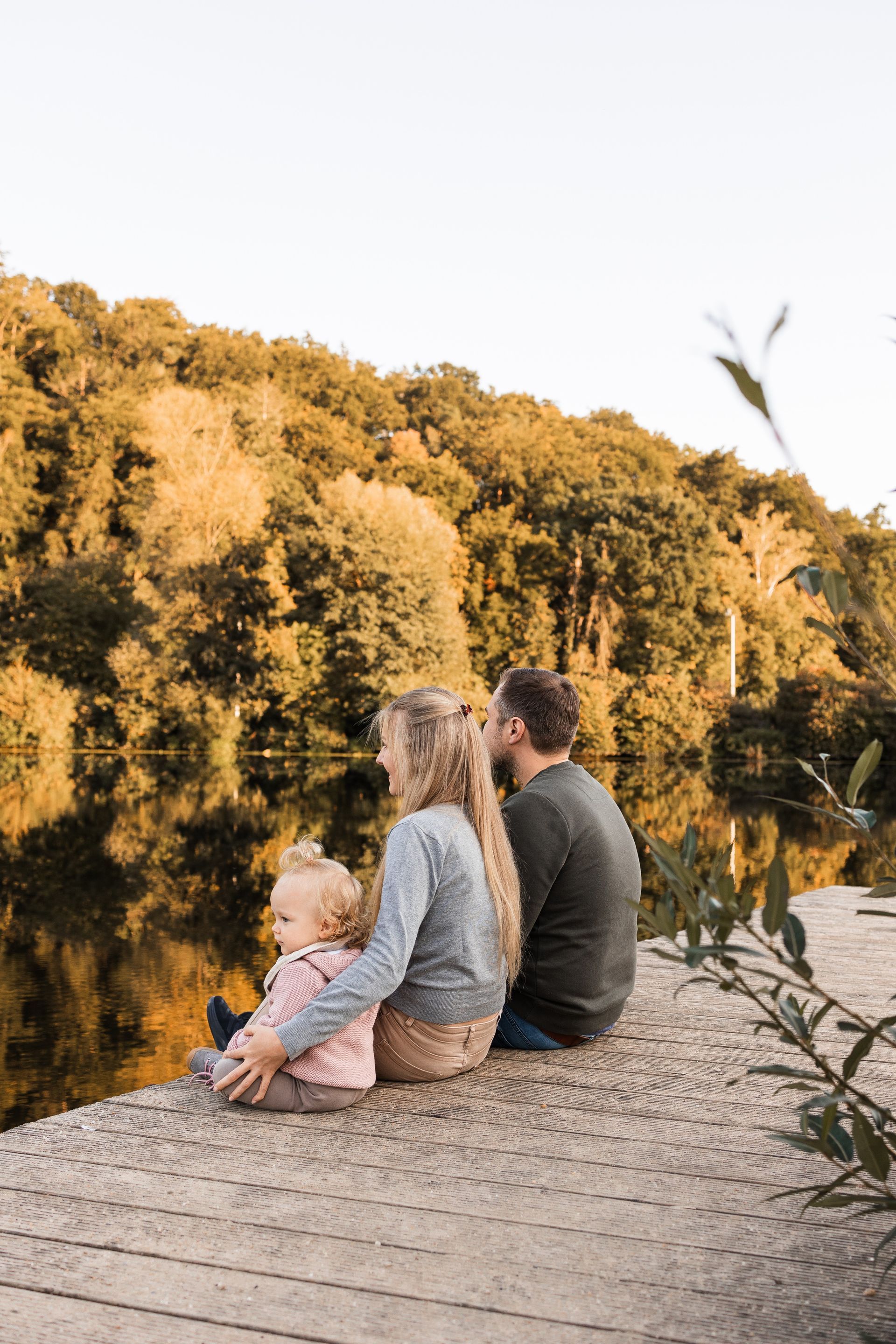 Auf diesem Bild sieht man eine Familie, die auf einem Steg am Wasser sitzt