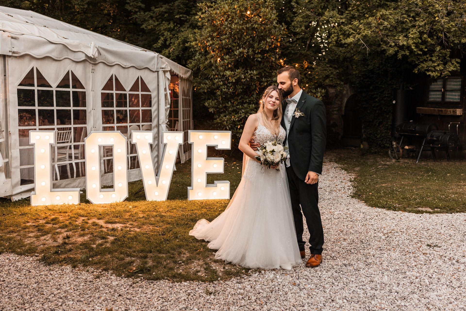 Auf diesem Foto steht ein Brautpaar vor leuchtenden LED Buchstaben