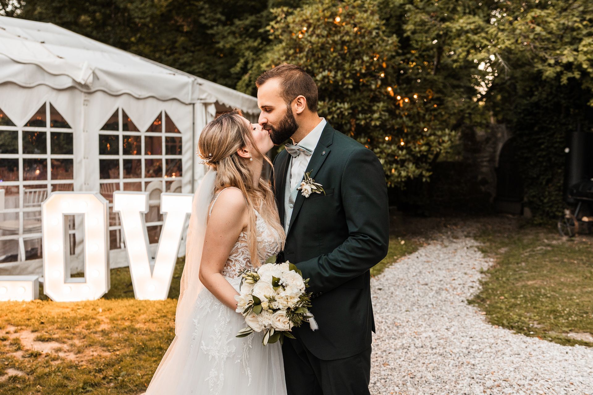 Auf diesem Foto küsst sich ein Brautpaar vor den LED Buchstaben