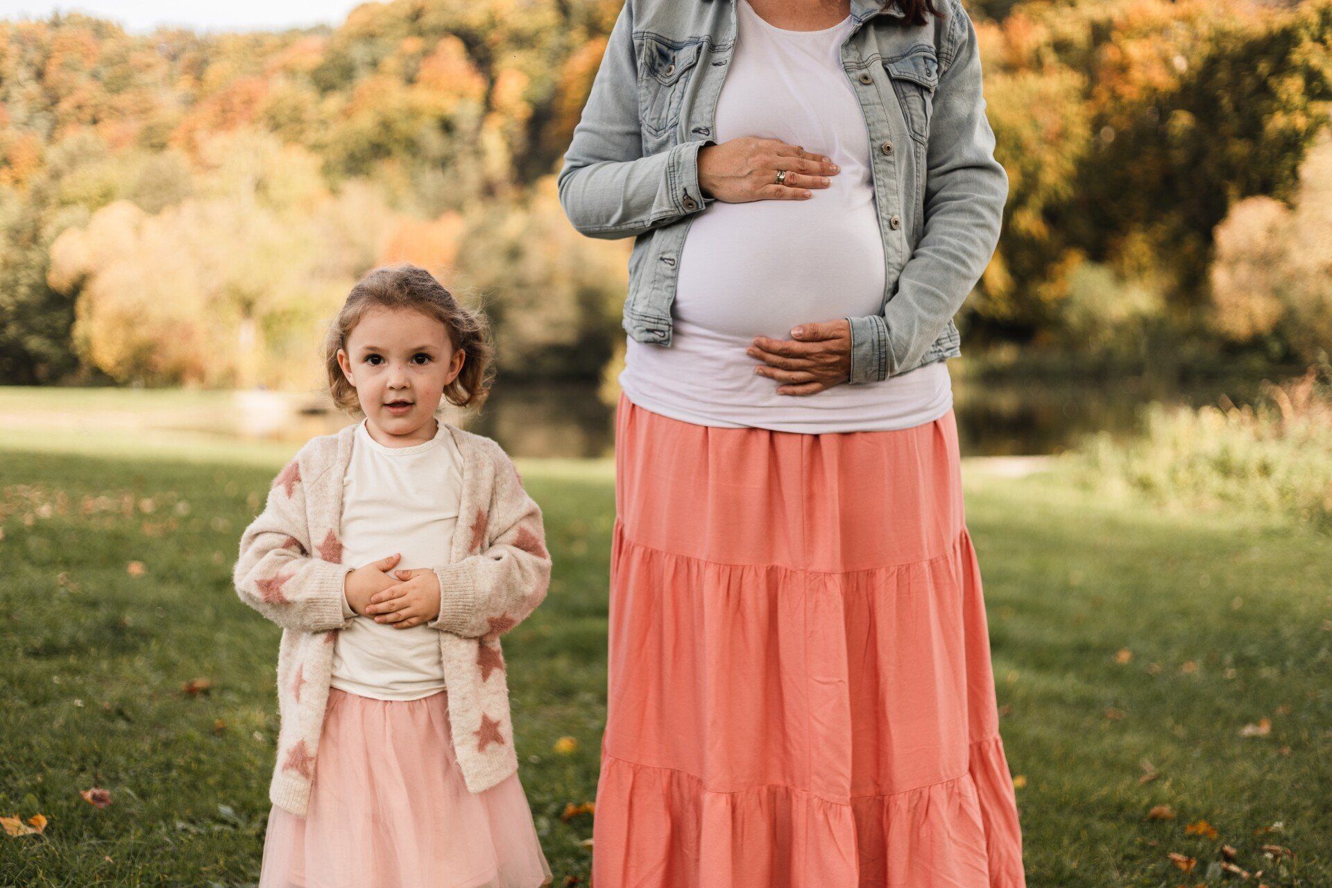 Süßes Bild von schwangerer Mutter und Tochter Auf diesem Foto sieht man die Mutter und ihre Tochter, die ihren Bauch halten