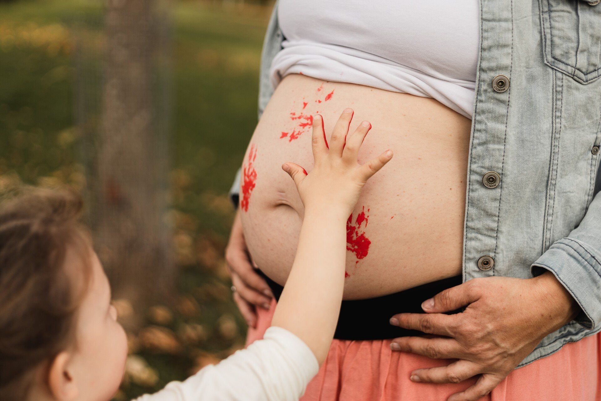 Farbige Abdrücke auf dem Babybauch Auf diesem Foto macht die Tochter Abdrücke aus Farbe auf den Babybauch der Mutter