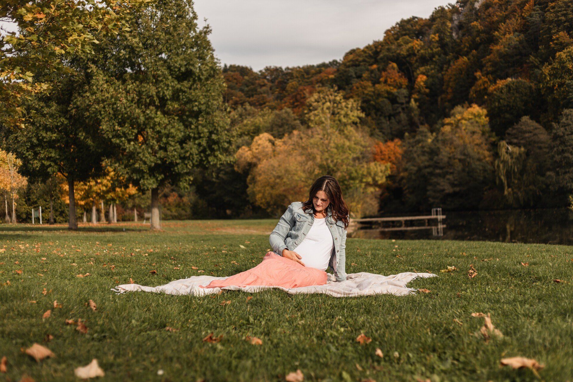 Schwangere Frau in der Natur auf einer Decke Auf diesem Bild sieht man eine schwangere Frau auf einer Picknickdecke auf einer Wiese am See