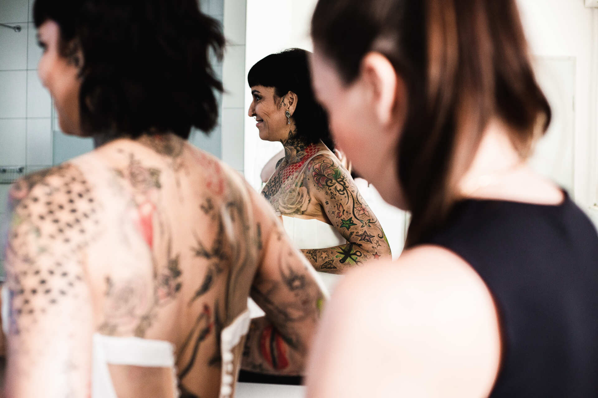 Braut während dem Getting Ready Man sieht die Braut im Spiegel, während ihr das Kleid angezogen wird