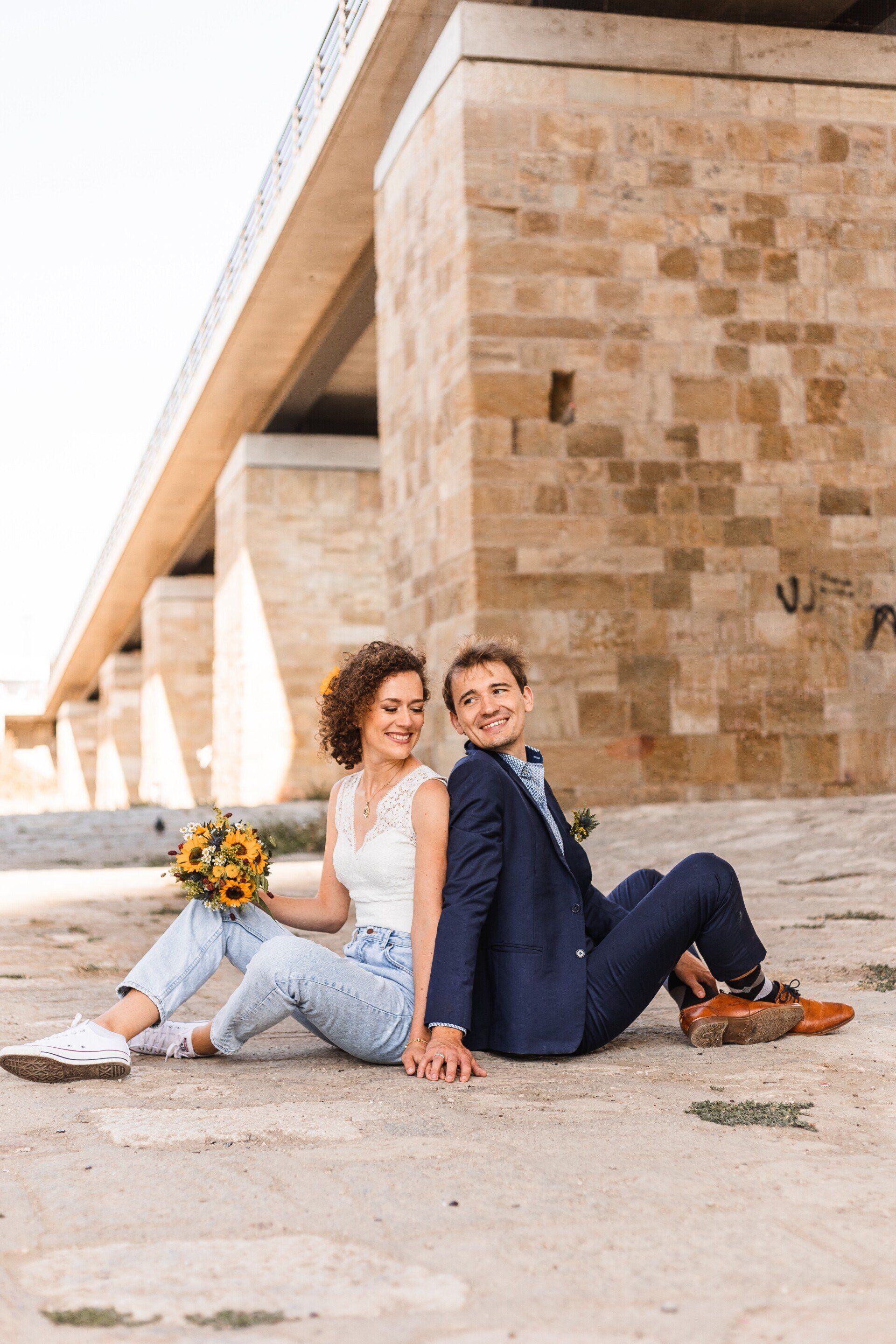 Auf diesem Foto sitzt ein Brautpaar auf dem Boden