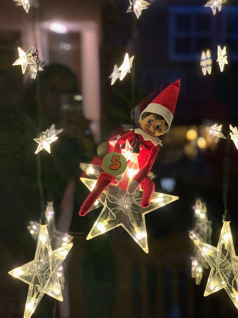 Elfo de els on the shelf colgando de una luz de navidad en forma de estrella