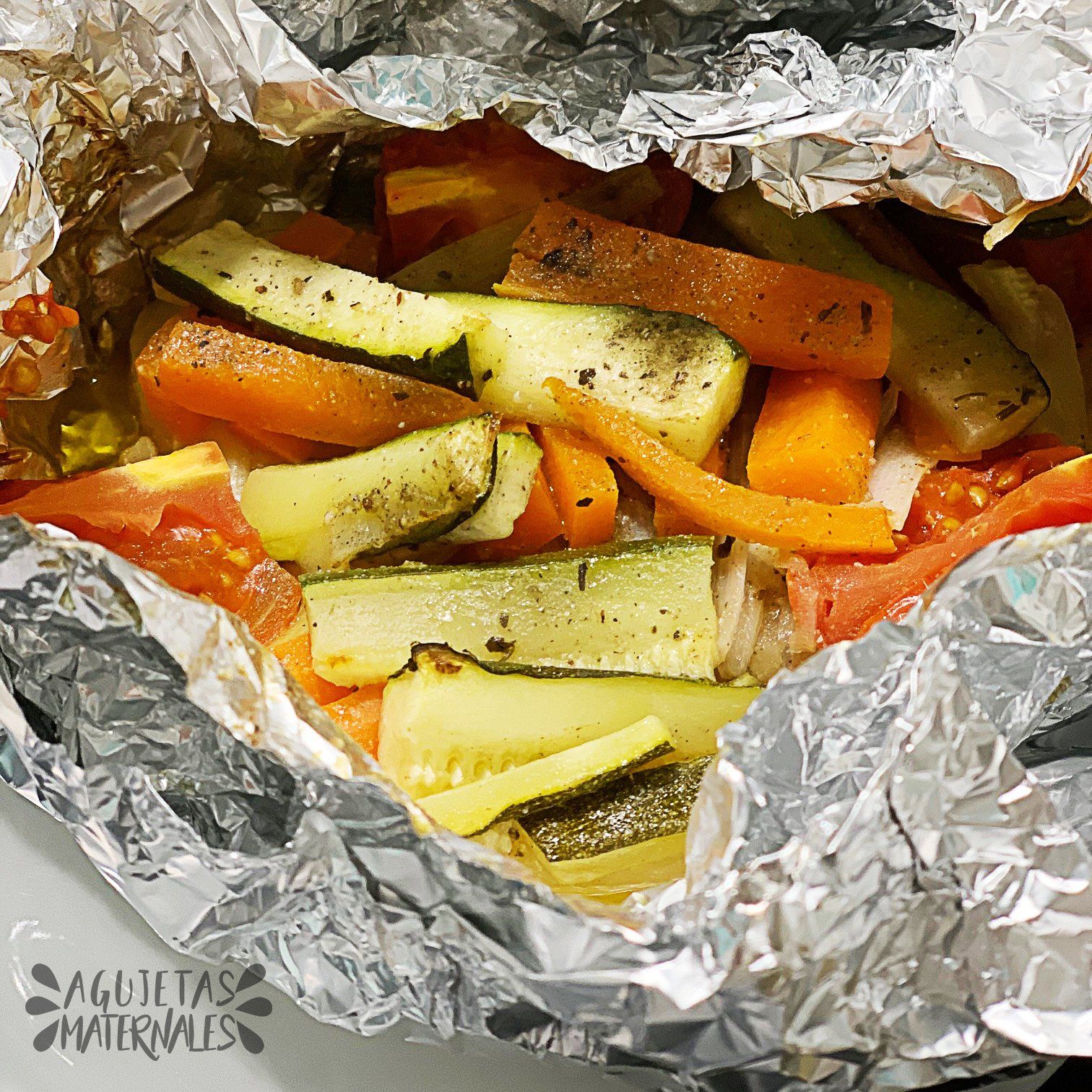 un saco de papel de plata y dentro verduras como calabacín, zanahoria, patata y tomate