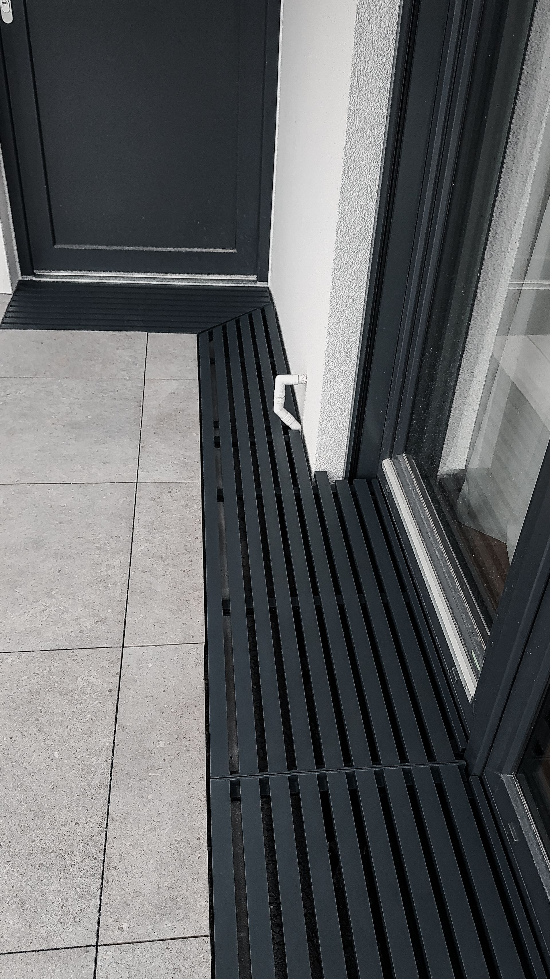 Maßgefertigtes Gitterrostsystem für ein modernes Fertighaus mit individuellen Ausschnitten für Fenster, Fassadenanschlüsse und Fallrohre. Verlegefertige Aluminium-Gitterroste mit passgenauer Konstruktion für Terrasse und Hauseingang.