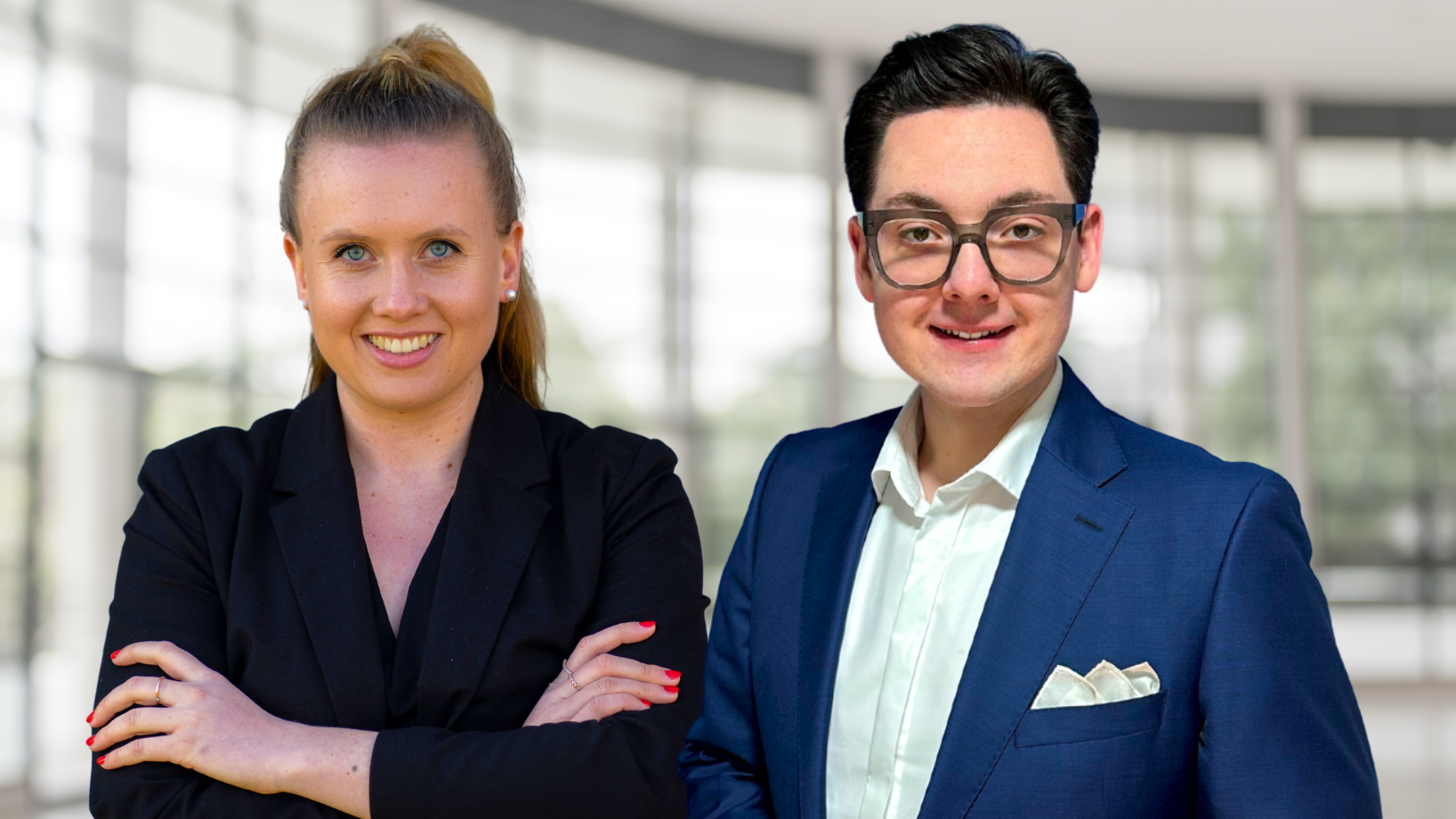 Die beiden Präsidiumsmitglieder der Bundesverbraucherhilfe – eine Frau im schwarzen Blazer mit verschränkten Armen und ein Mann im blauen Anzug mit Einstecktuch – stehen selbstbewusst nebeneinander vor einem lichtdurchfluteten, modernen Besprechungsraum und blicken direkt in die Kamera.