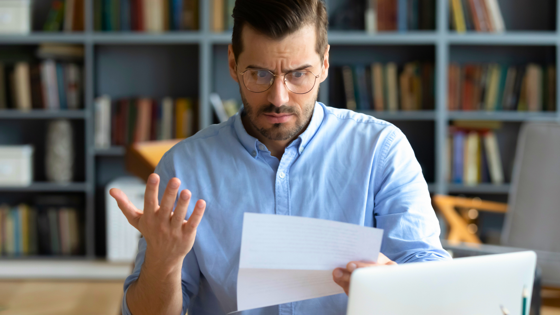 Ein Mann mit Brille sitzt an einem Schreibtisch vor einem Laptop und hält ein amtlich wirkendes Schreiben in der Hand. Mit ernster Miene und fragender Geste reagiert er sichtbar irritiert auf den Inhalt. Das Bild vermittelt das Gefühl von Frust oder Unverständnis – etwa nach Erhalt eines fehlerhaften Bescheids oder einer unklaren Rechnung.
