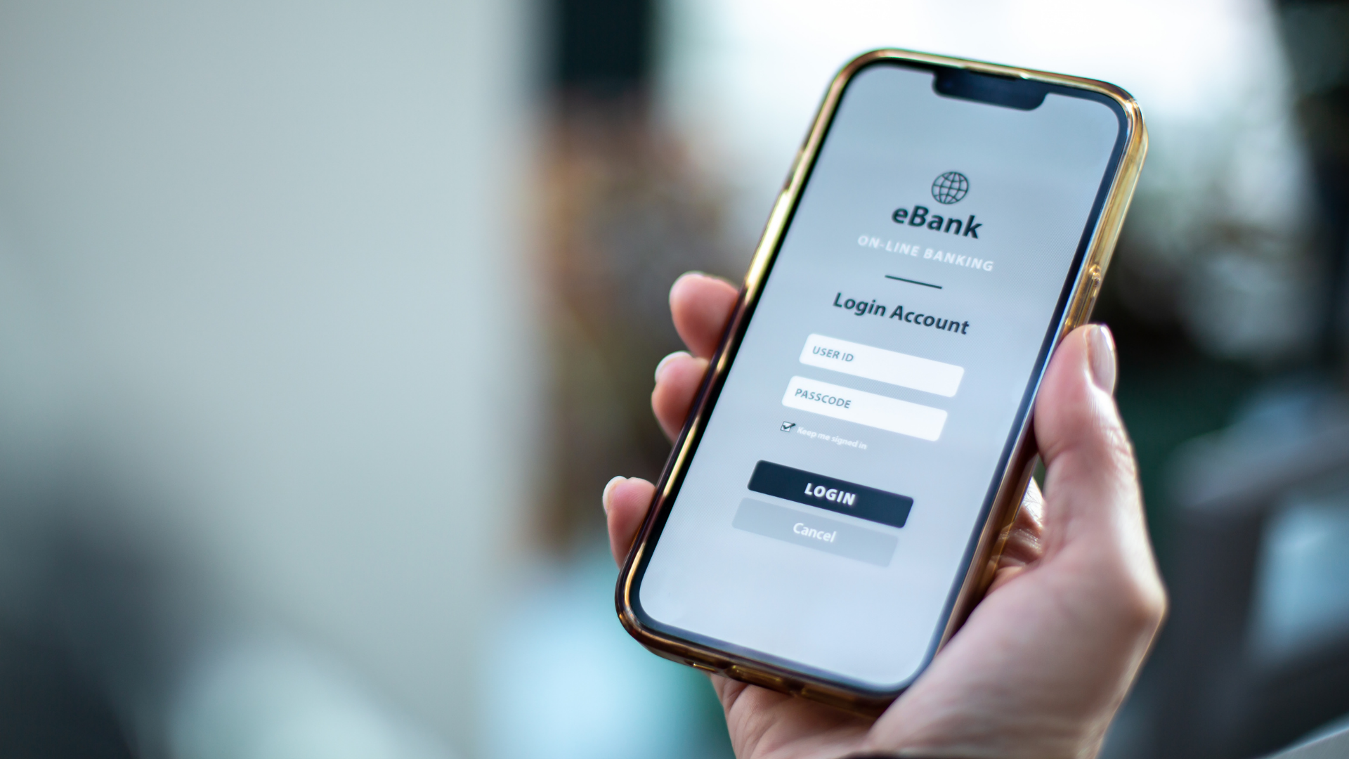 Das Bild zeigt eine Hand, die ein Smartphone hält, auf dessen Bildschirm die Login-Seite einer Online-Banking-App angezeigt wird. Auf dem Display sind Felder für die Benutzer-ID und den Passcode zu sehen, sowie ein
