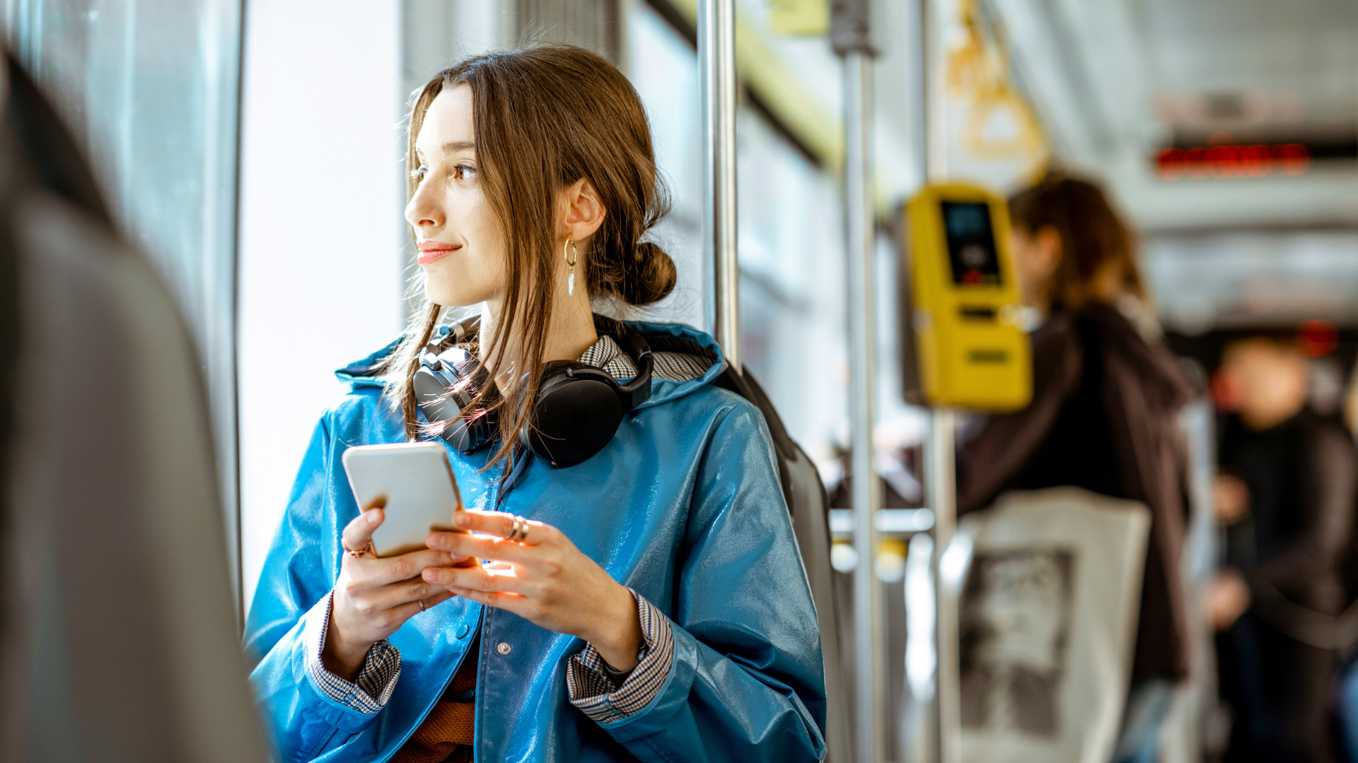 Eine Frau mit Kopfhörern und Smartphone steht im Bus und blickt nach draußen. Die Szene zeigt Mobilität im Alltag, Selbstbestimmung und moderne Fortbewegung.